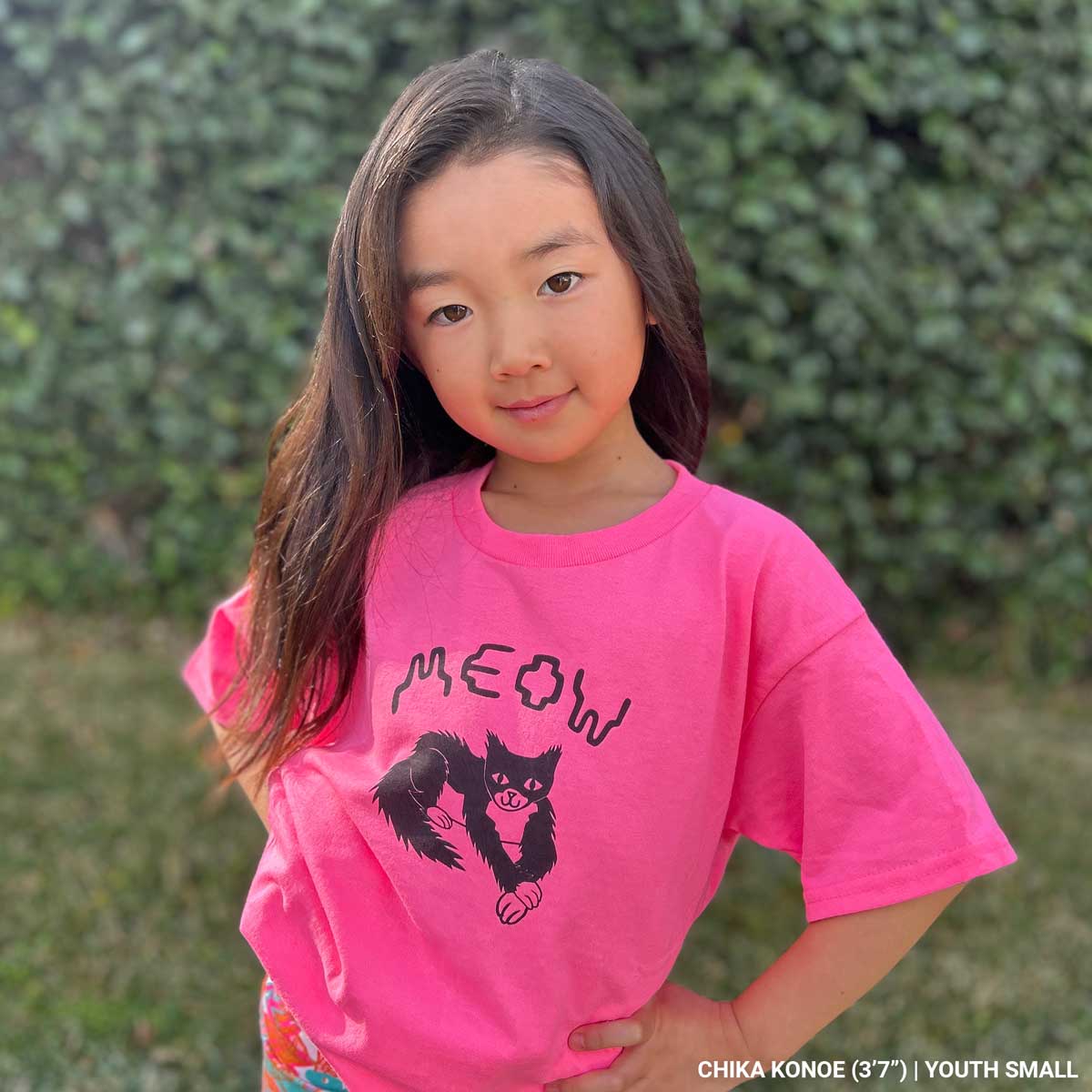 Child wearing a pink t-shirt with a black cat graphic and 'MEOW' text, standing outdoors.