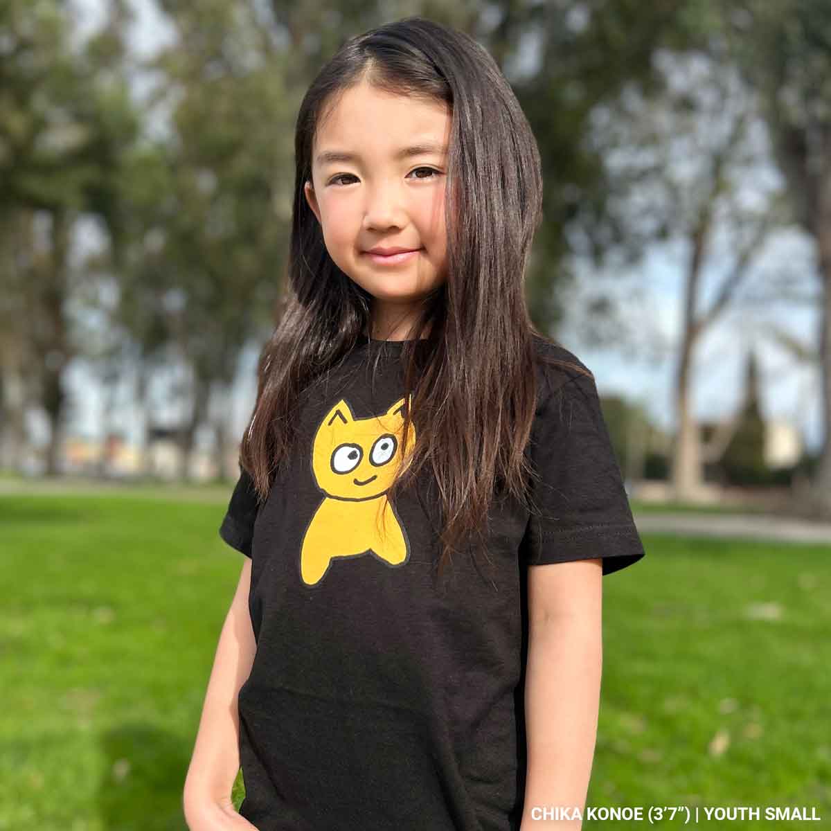 Young girl wearing a black t-shirt with a yellow cat graphic in an outdoor setting