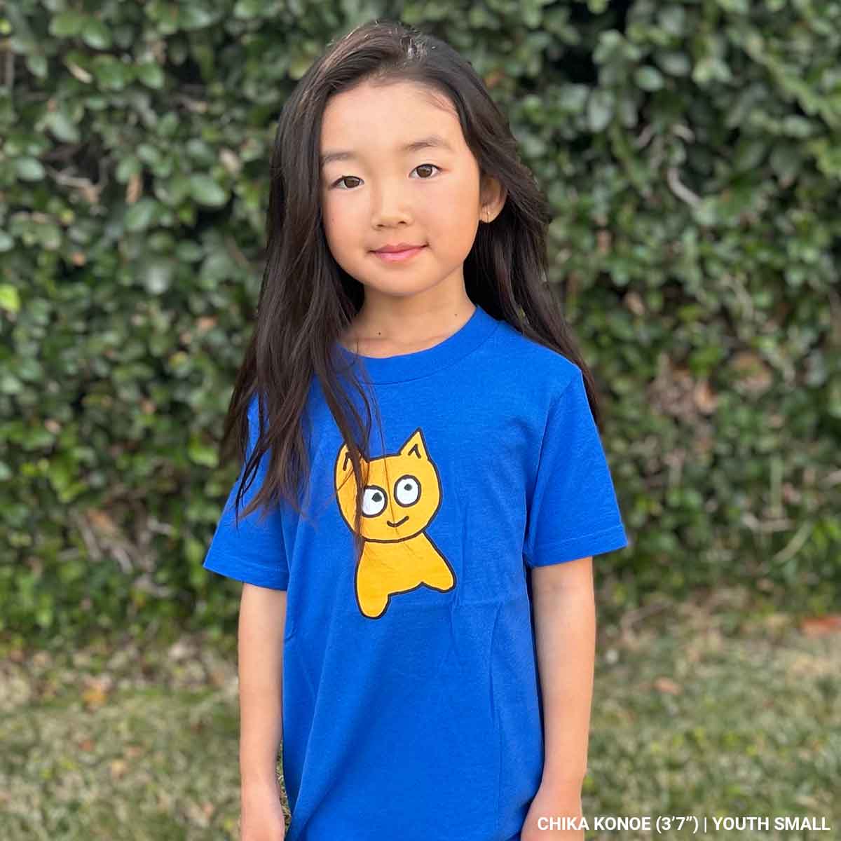 Child wearing a blue t-shirt with a yellow cartoon cat against a green leafy background