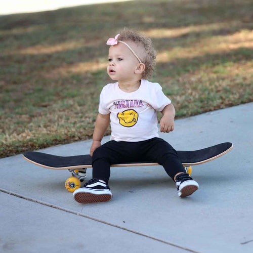 toddler sitting on a soft top skateboard on a sidewalk